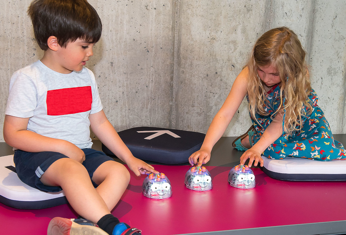 Zwei Kinder drücken die Startknöpfe mehrerer Robotik-Spielzeuge, die wie gläserne Mäuse aussehen.