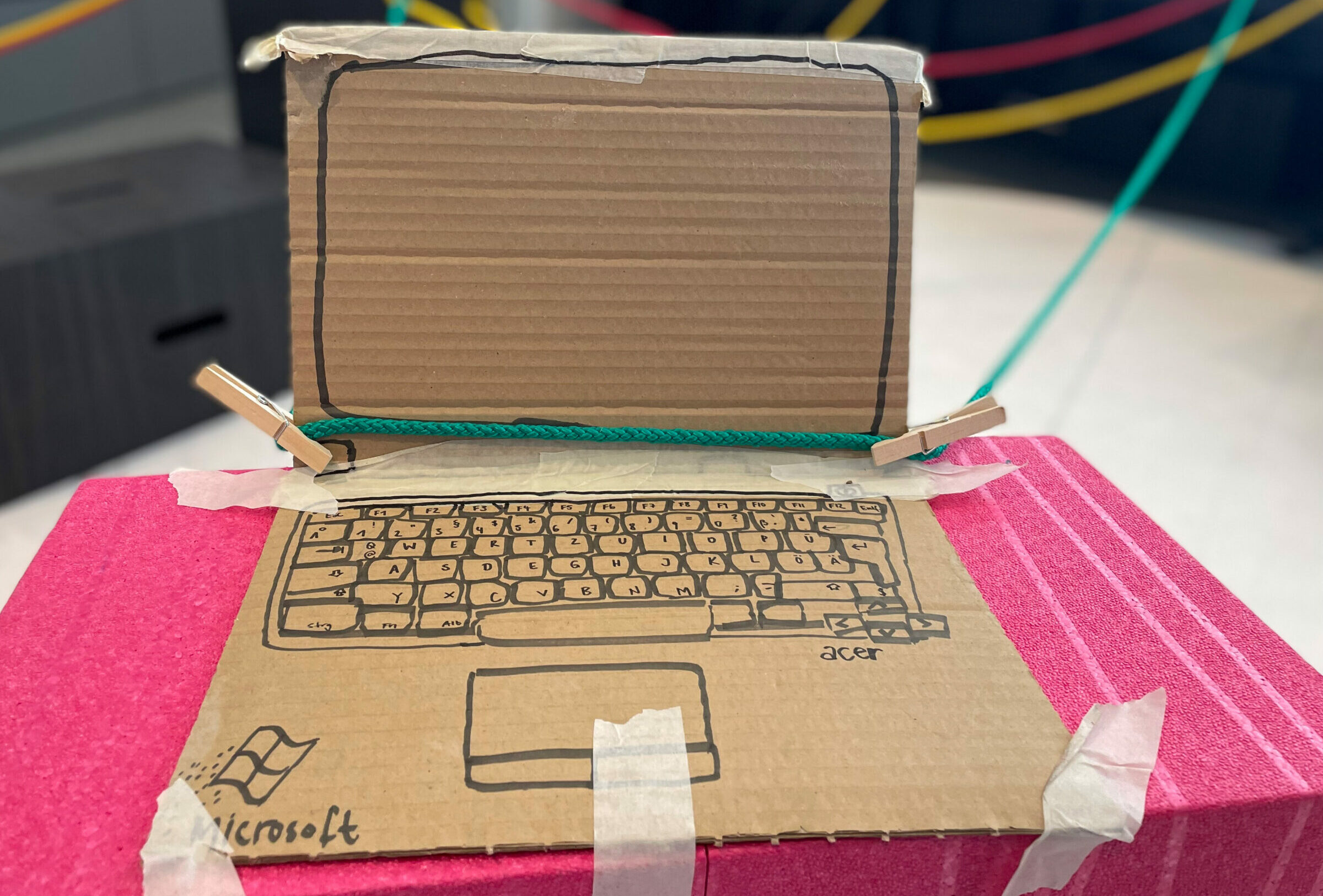 Ein aus Pappe gebastelter Laptop, der mit bunten Seilen verbunden ist.